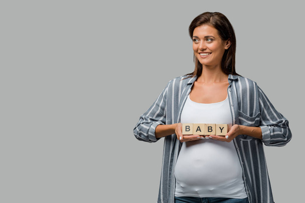 cheerful pregnant woman holding alphabet cubes with baby sign, isolated on grey - Fotó, kép