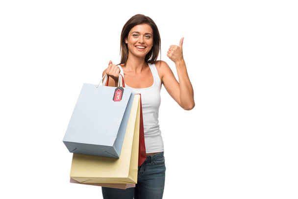 beautiful girl holding shopping bags with sale signs while showing thumb up, isolated on white  - Photo, Image