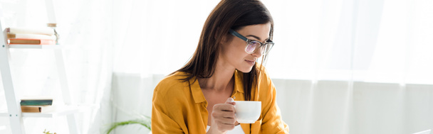 Gözlüklü serbest çalışan güzel bir kadın. Ofiste elinde bir fincan kahve tutuyor. - Fotoğraf, Görsel