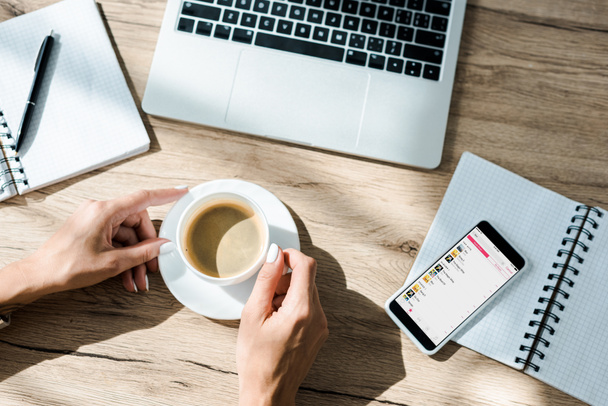 KYIV, UKRAINE - SEPTEMBER 10, 2019: cropped view of freelancer with cup of coffee, laptop and smartphone with apple music app  - Foto, Imagem