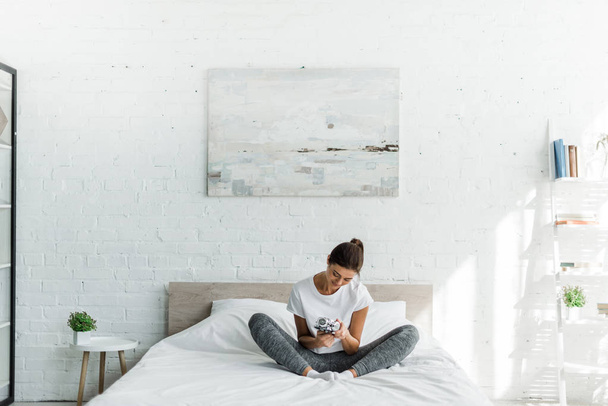 happy girl sitting with alarm clock on bed in the morning - Φωτογραφία, εικόνα