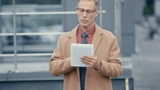 przystojny biznesmen w płaszczu za pomocą tabletu cyfrowego  - Materiał filmowy, wideo