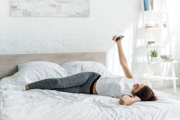 attractive girl taking selfie on smartphone while lying on bed - Fotoğraf, Görsel