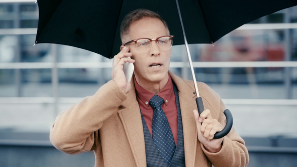 сердитий бізнесмен тримає парасольку і розмовляє на смартфоні
  - Кадри, відео