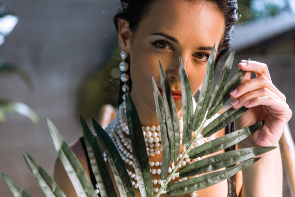 attractive woman in earrings with plant looking at camera  - Fotografie, Obrázek
