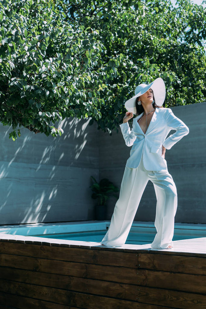 attractive woman in white suit and hat posing outside  - Фото, зображення