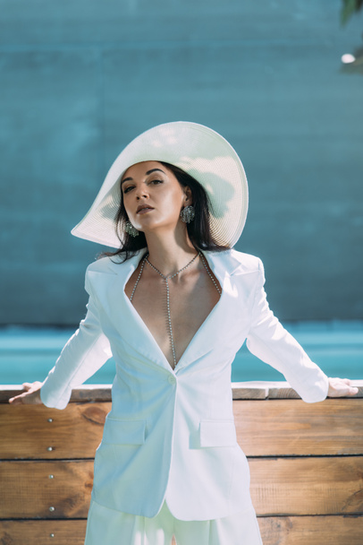 attractive woman in white suit and hat posing and looking at camera outside  - 写真・画像