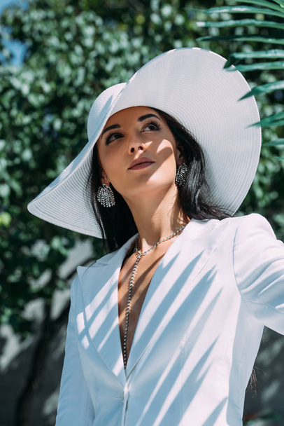 attractive woman in white suit and hat posing and looking away outside  - Φωτογραφία, εικόνα