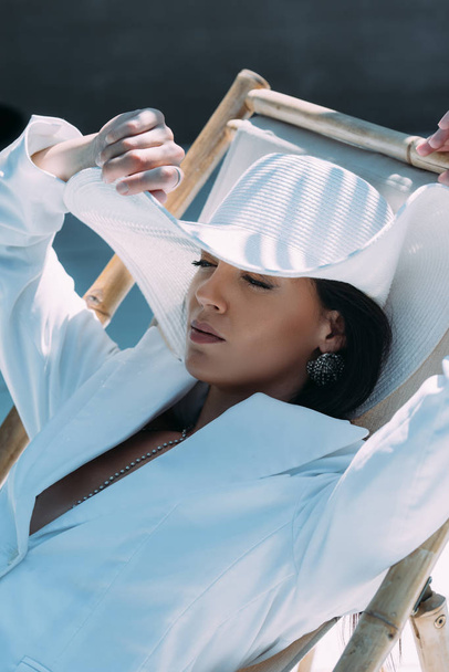 jolie femme en costume blanc et chapeau posant avec les yeux fermés à l'extérieur
  - Photo, image