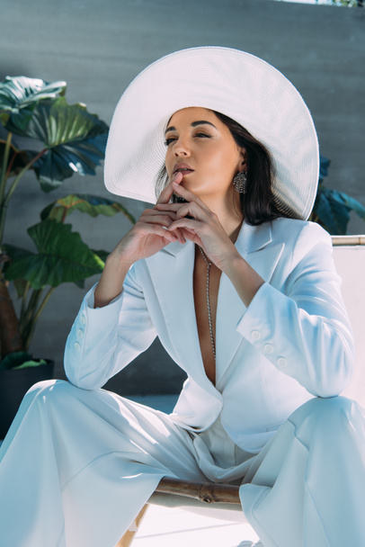 attractive woman in white suit and hat posing and looking away outside  - Фото, изображение
