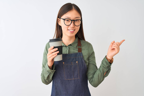 Kiinalainen barista nainen yllään esiliina lasit kahvin yli eristetty valkoinen tausta erittäin onnellinen osoittaa käsin ja sormella sivulle
 - Valokuva, kuva