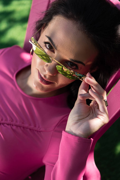 привлекательная женщина в платье и солнцезащитных очках позирует и смотрит в камеру снаружи
  - Фото, изображение