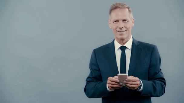 hombre de negocios en traje sonriendo y usando teléfono inteligente
  - Metraje, vídeo