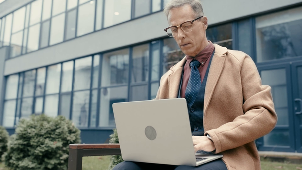 üzletember kabátban és szemüvegben laptoppal  - Felvétel, videó
