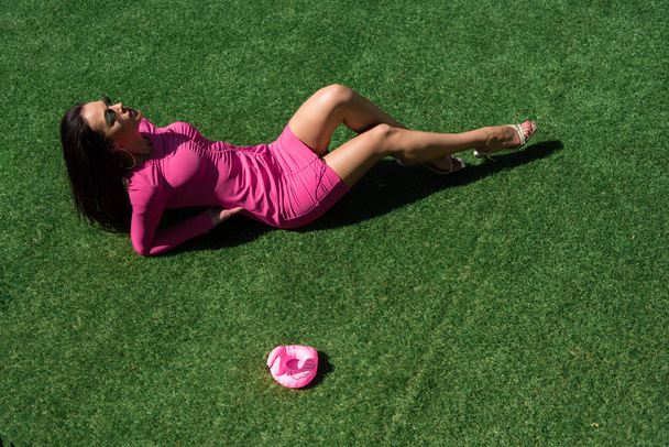 外の芝生の上でポーズをとって横になるドレスやサングラスの魅力的な女性の高い角度の眺め  - 写真・画像