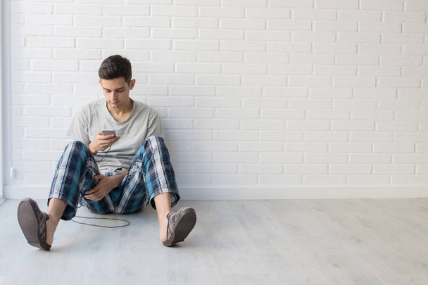 молодой человек на полу дома с мобильным телефоном
 - Фото, изображение