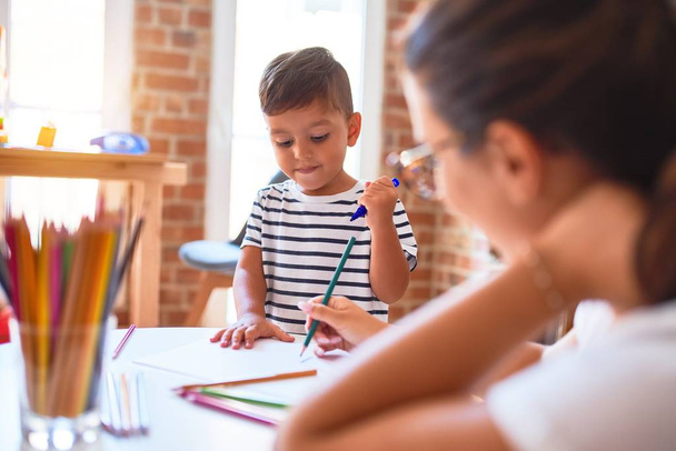 Piękny nauczyciel i maluch rysunek chłopiec przy użyciu kolorowych ołówków w przedszkolu - Zdjęcie, obraz