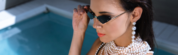 plan panoramique de femme séduisante en lunettes de soleil posant près de la piscine
  - Photo, image