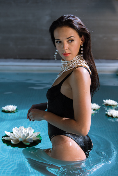 mulher atraente em maiô preto e colar de pérolas posando na piscina
  - Foto, Imagem