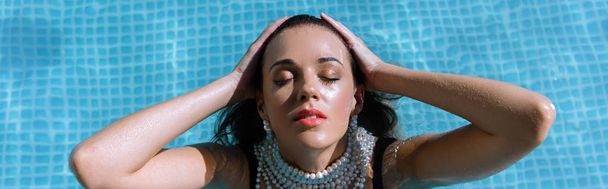 プールでポーズをとる真珠のネックレスの魅力的な女性のパノラマショット  - 写真・画像