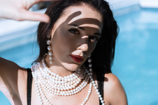 attractive woman in pearl necklace posing in pool and looking at camera  - Foto, immagini