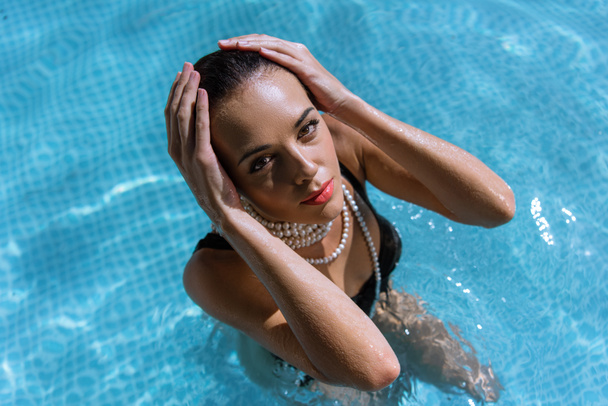 Siyah mayo ve havuzda poz veren inci kolyeli çekici bir kadının yüksek açılı görüntüsü.  - Fotoğraf, Görsel