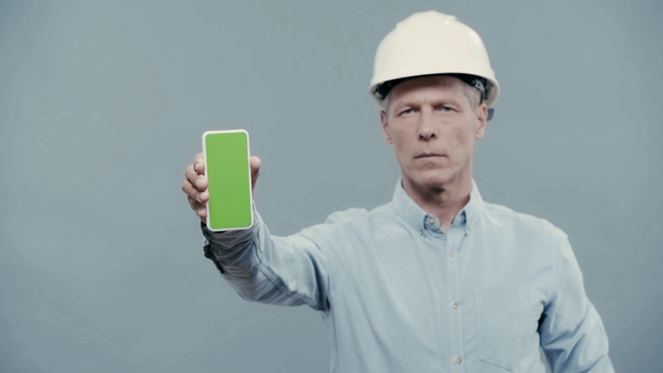 αρχιτέκτονας σε κράνος δείχνει smartphone με κενή οθόνη - Πλάνα, βίντεο