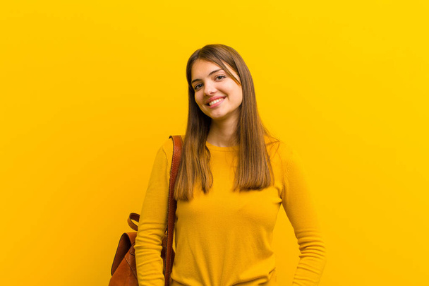 young pretty woman smiling cheerfully and casually with a positive, happy, confident and relaxed expression against orange background - Фото, изображение