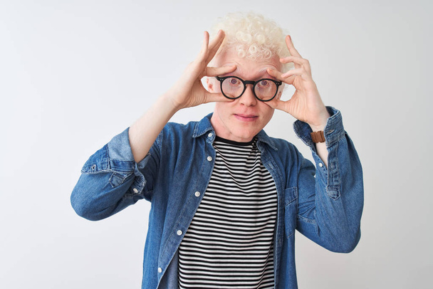 Young albino blond man wearing denim shirt and glasses over isolated white background Trying to open eyes with fingers, sleepy and tired for morning fatigue - Photo, Image