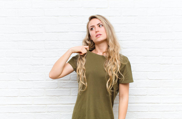 young blonde woman feeling stressed, anxious, tired and frustrated, pulling shirt neck, looking frustrated with problem against brick wall background - Foto, imagen
