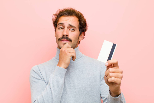 fiatal jóképű férfi egy hitelkártya ellen rózsaszín lapos fal - Fotó, kép