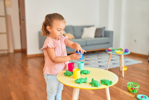 Красивая блондинка девочка играет с пластиковыми лягушками игрушки в детском саду
 - Фото, изображение
