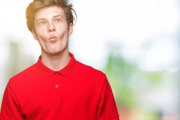 Jonge knappe man met rode t-shirt over geïsoleerde achtergrond maken vis gezicht met lippen, gek en komische gebaar. Grappige expressie. - Foto, afbeelding