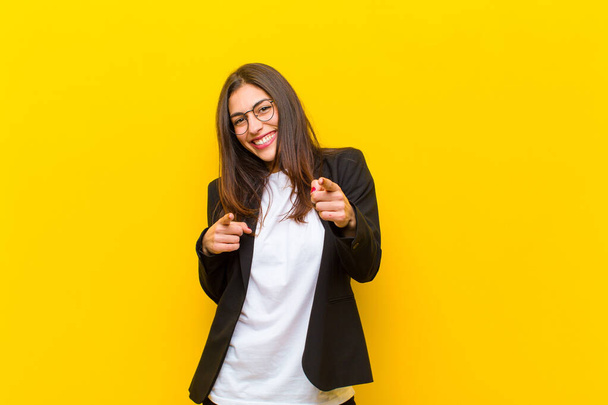 young  pretty woman smiling with a positive, successful, happy attitude pointing to the camera, making gun sign with hands against orange wall - Foto, immagini
