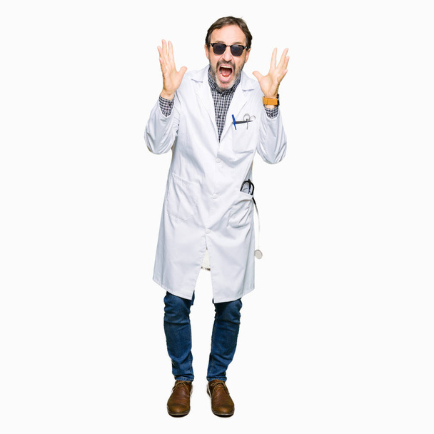 Красивый врач средних лет в солнцезащитных очках празднует безумный и безумный успех с поднятыми руками и с взволнованными закрытыми глазами. Концепция победителя
 - Фото, изображение