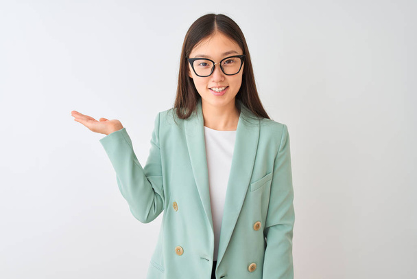 Čínská podnikatelka na sobě elegantní bunda a brýle na izolovaném bílém pozadí s úsměvem veselý prezentaci a ukazuje dlaní ruky při pohledu do kamery. - Fotografie, Obrázek