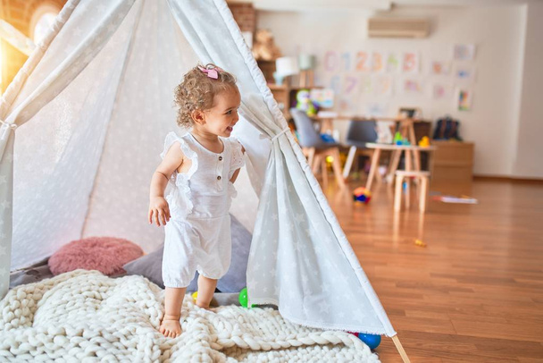 Kaunis valkoihoinen pikkulapsi leikkii leluilla värikkäässä leikkihuoneessa. Iloinen ja leikkisä intialainen teltta päiväkodissa
. - Valokuva, kuva