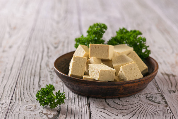 hliněný talíř s tofu a kudrnatými petrželovými listy na dřevěném stole. - Fotografie, Obrázek