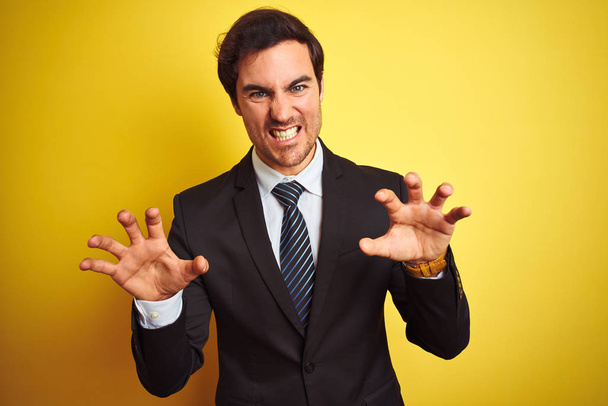 Young handsome businessman wearing suit and tie standing over isolated yellow background smiling funny doing claw gesture as cat, aggressive and sexy expression - Zdjęcie, obraz