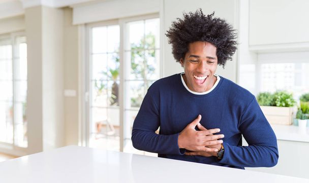 Young african american man wearing casual sweater sitting at home smiling and laughing hard out loud because funny crazy joke with hands on body. - Foto, immagini