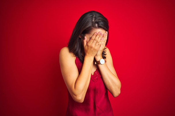 Jonge mooie vrouw dragen sexy lingerie over rood geïsoleerde achtergrond met droevige uitdrukking bedekken gezicht met handen tijdens het huilen. Depressieconcept. - Foto, afbeelding