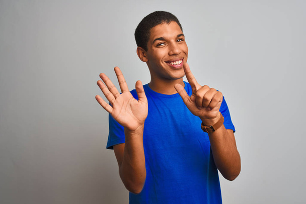 Молодой красивый арабский мужчина в голубой футболке стоит на изолированном белом фоне и показывает пальцами номер семь, улыбаясь уверенно и счастливо
. - Фото, изображение
