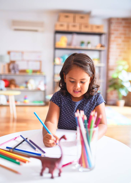 Красива дівчинка малює милий малюнок, використовуючи кольорові олівці в дитячому саду
 - Фото, зображення