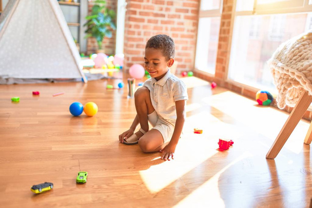 Beautiful african american toddler playing with cars around lots of toys at kindergarten - Foto, imagen