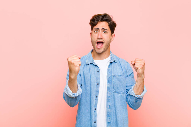 young handsome man shouting triumphantly, looking like excited, happy and surprised winner, celebrating against pink background - Fotografie, Obrázek