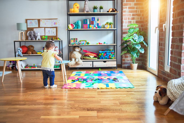 Gyönyörű kisbaba áll körül sok játékok óvodában - Fotó, kép