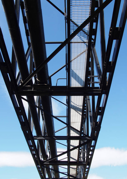 vista de perspectiva de un puente de tubería de acero industrial construido para transportar agua y gas a través de un río con una pasarela de acceso para el mantenimiento contra un cielo azul nublado
 - Foto, Imagen