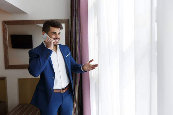 Attractive businessman talking by phone near window in hotel - Фото, зображення
