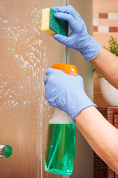 Main de femme âgée utilisant une éponge avec un détergent pour nettoyer la douche en verre, concept de tâches ménagères
 - Photo, image