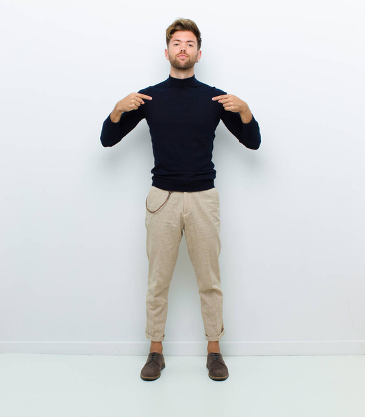 young full body man looking proud, positive and casual pointing to chest with both hands against white background - Fotó, kép
